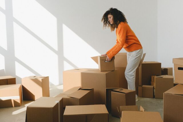 Cutii de mutare stivuite într-un apartament luminos, lângă o plantă și o canapea încă neacoperită