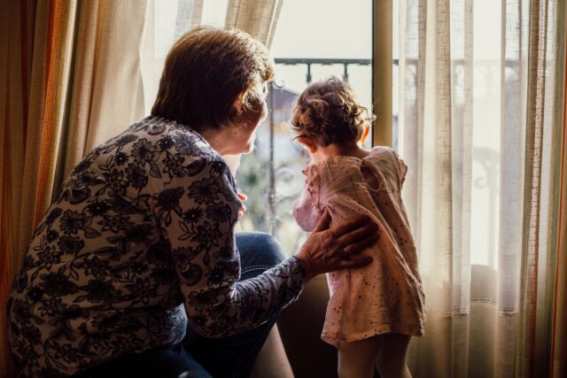 O bunică și nepoțica ei care frământă aluat împreună într-o bucătărie luminoasă, cu făină pe masă