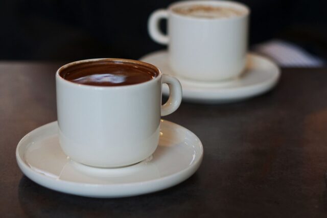 Două cești de cafea pe o măsuță de cafenea, lângă fereastră, pregătite pentru o primă întâlnire